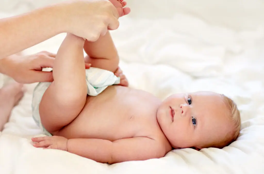 Cute baby having his nappy changed while lying on a soft bed